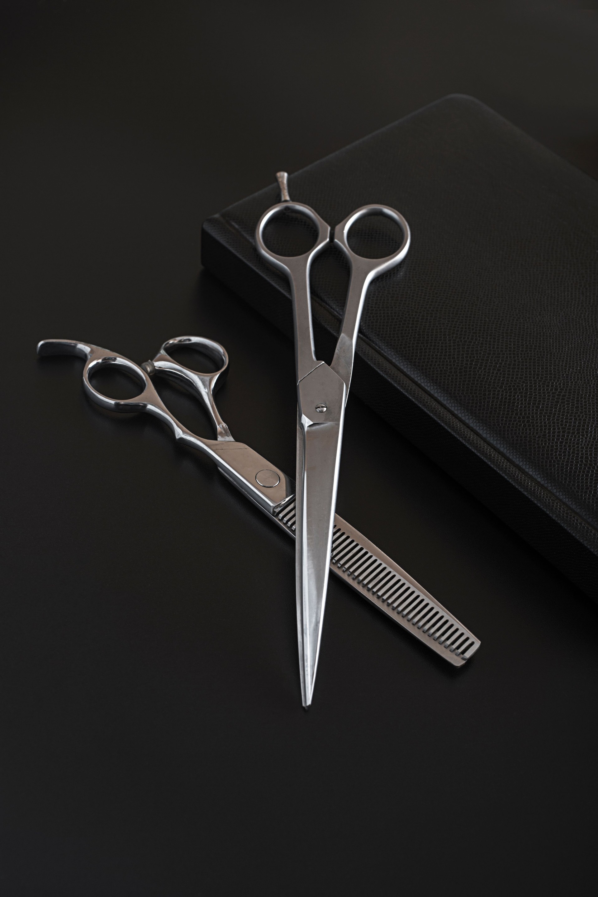 Friseur- oder Pflegeschere und Notizbuch Tagebuch auf schwarzem Hintergrund. Friseur oder Pflegeschere und Tagesplaner Nahaufnahme. Friseurbuch zum Schreiben von Kunden.